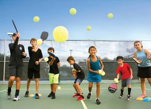 Seven young players practicing with paddles and balls on an outdoor court